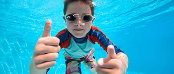 Kid underwater with goggles giving the thumbs up