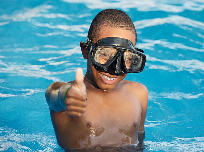 Boy in pool with goggles on giving a thumbs up