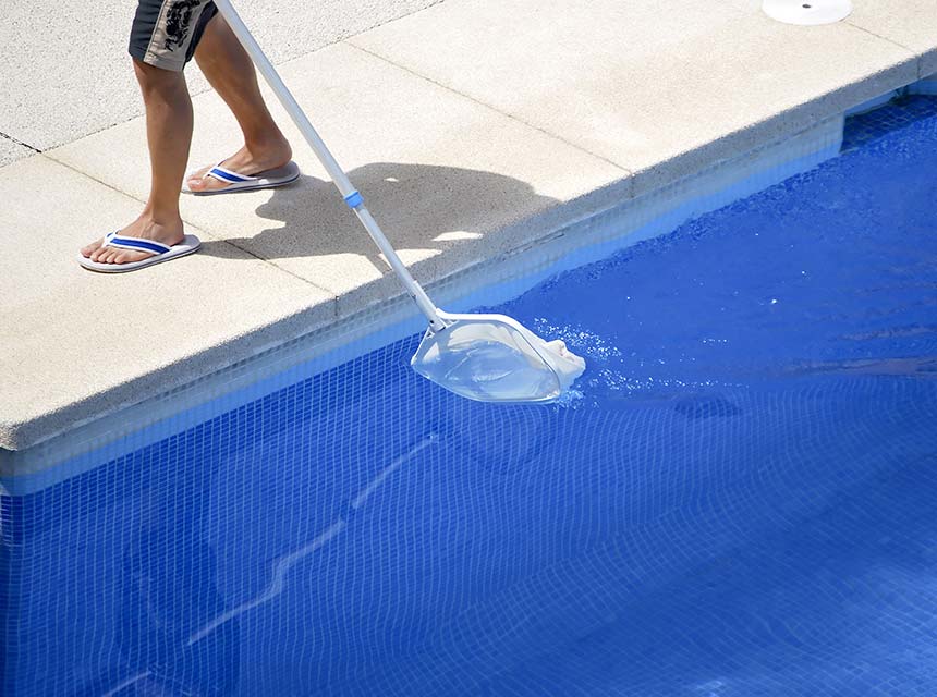 Man in sandals cleaning pool with pool net